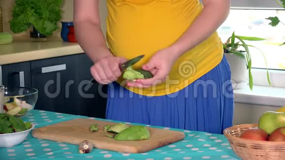孕妇肚子和手在厨房里剥掉鳄梨水果视频的预览图
