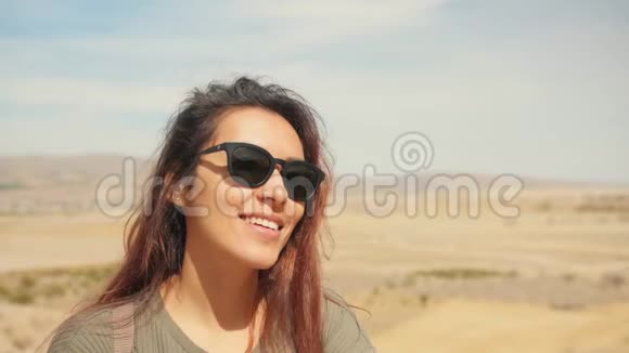 年轻迷人的微笑混合赛车女孩的肖像在沙漠快乐的旅游妇女在镜头上摆姿势头发在风中飘扬视频的预览图
