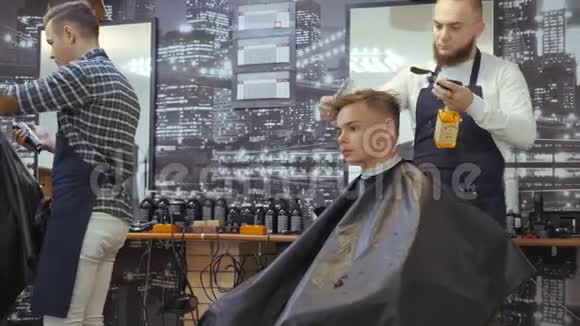 男士美容师理发店一个年轻人从一个头发被绑在头上的留着胡子的男人那里得到理发和头发护理视频的预览图