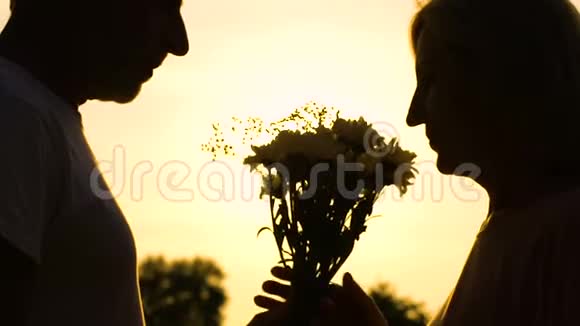 一位年长的男人带着女人的花在夕阳的背景下亲吻她的手视频的预览图