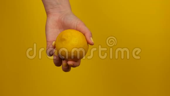 有黄色指甲的女性手在黄色背景上拿着柠檬视频的预览图