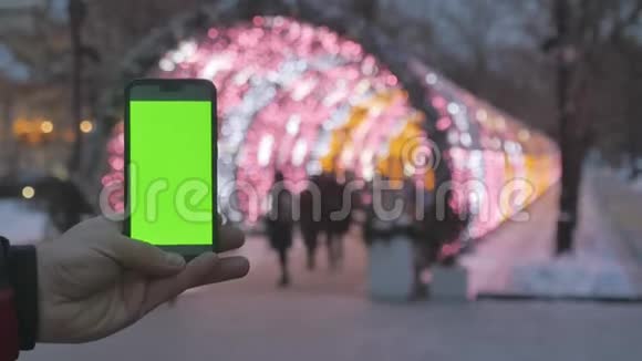 带有绿色屏幕的智能手机在背景中新年彩色花环失去了焦点视频的预览图