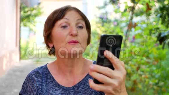 使用黑色智能手机进行在线视频聊天的老年妇女视频的预览图