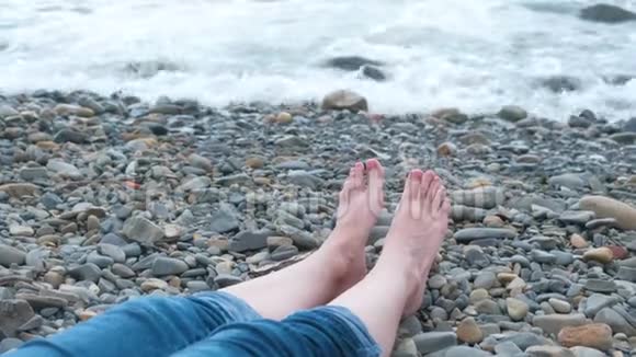 女人脚穿牛仔裤靠在沙滩上的海边视频的预览图
