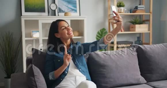有魅力的女孩在家里坐在沙发上用智能手机拍照视频的预览图