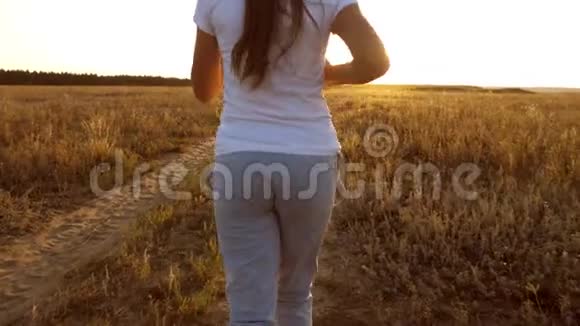 美丽的女孩在乡村日落时做体育锻炼戴着耳机的女孩沿着路跑听着视频的预览图