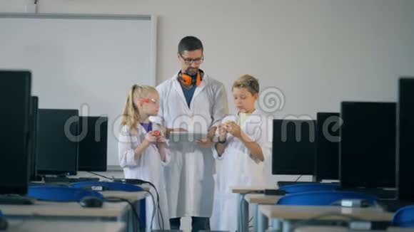 男的实验室工作人员和两个孩子站在电脑室里观察多余的细节视频的预览图