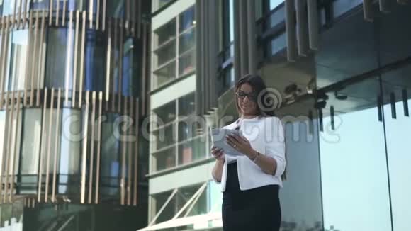 年轻漂亮的女律师正在使用平板电脑站在办公楼的背景上视频的预览图