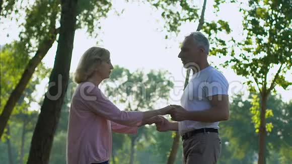幸福的老夫妇牵着手在美丽的绿色公园里跳舞慢动作视频的预览图