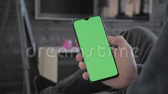 绿色屏幕男人坐在沙发上看智能手机视频的预览图