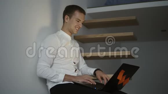 一位年轻的职业男性自由职业者穿着白色衬衫坐在现代电脑前使用笔记本电脑视频的预览图