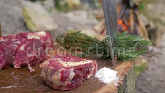 在篝火的背景下在木块上撒上多汁的猪肉锉用来煮牛排视频的预览图