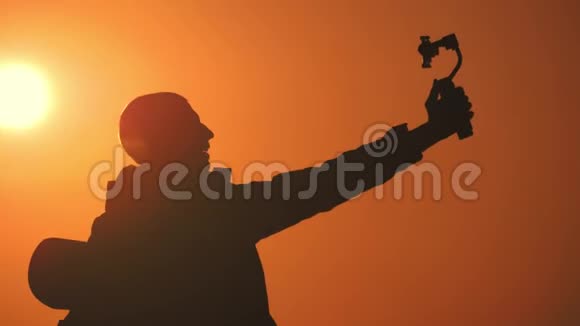剪影男子游客手持稳定相机与一个电话在日落背景视频的预览图