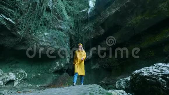 年轻美丽的白种人女孩旅行者穿着黄色雨衣穿过一个热带洞穴在这里寻找冒险视频的预览图