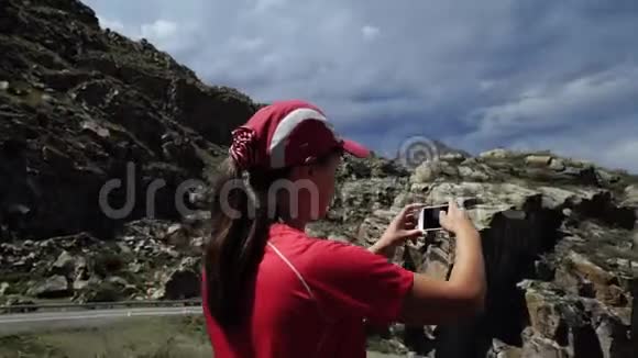 年轻快乐的旅行女孩带着背包和帽子到达山的边缘拍照风景优美视频的预览图