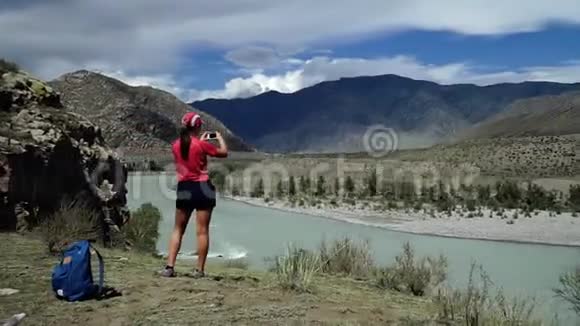 旅行女孩带着背包和帽子到达山的边缘并拍照后视滑块视频的预览图