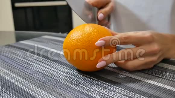 年轻的女性手在家厨房的桌子上切割成熟多汁的橘子视频的预览图