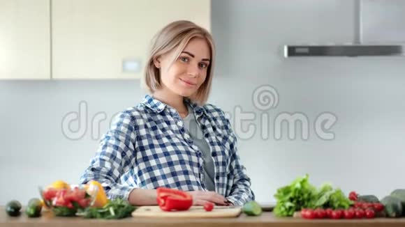 美丽的年轻休闲家庭主妇在烹饪健康食品时摆姿势看着相机视频的预览图