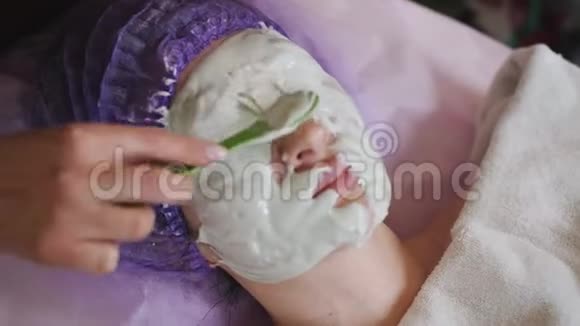 美容院戴面膜的漂亮女人美容师用绿色面膜敷脸皮肤程序视频的预览图