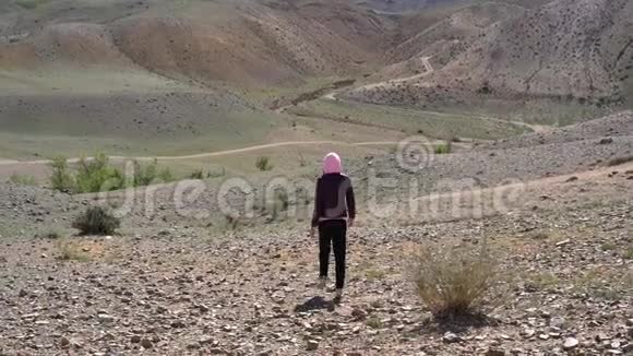这个女孩正沿着一片荒凉的石头地形在山丘和山脉的背景下行走视频的预览图