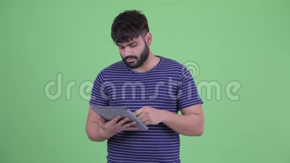快乐年轻体重超重留胡子的印度男人使用数码平板电脑视频的预览图