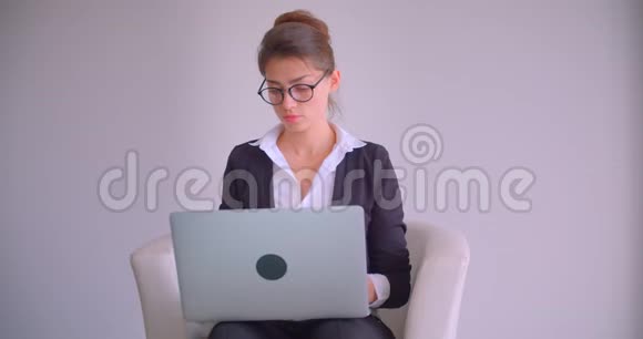 一位年轻漂亮的白种人女商人用笔记本电脑在室内的办公室里看着照相机的特写镜头视频的预览图
