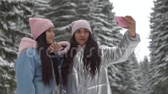 两个心情好的女朋友在冬天的森林里站着用智能手机自拍慢动作视频的预览图