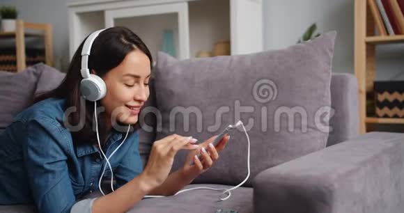 可爱的年轻女士用耳机触摸智能手机屏幕听音乐视频的预览图