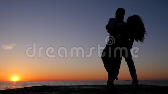 西班牙年轻夫妇在日落海背景下的剪影男人和女人跳舞拉丁美洲性感舞蹈视频的预览图