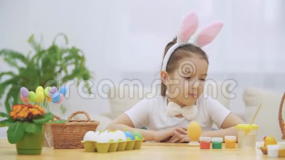 可爱的小女孩头上戴着小兔子的耳朵正在选择一种红色来画一个鸡蛋视频的预览图
