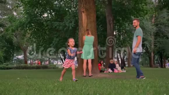 年轻的一家人夏天在公园里散步玩捉迷藏女儿在找地方躲起来视频的预览图