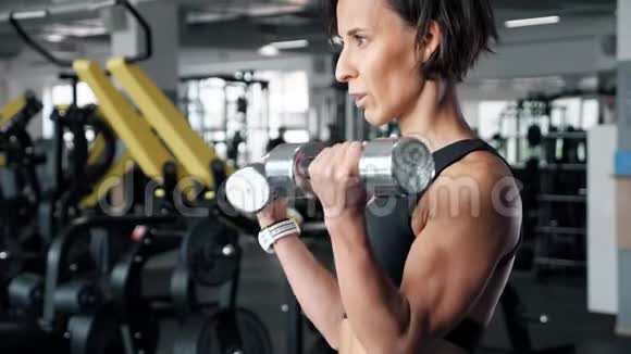 运动成熟的女人正在健身房用哑铃做二头肌运动视频的预览图