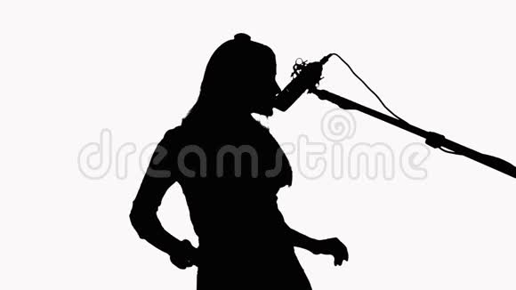 一个长发女孩的剪影她对着录音棚的麦克风唱歌在白色背景上录制音乐视频视频的预览图