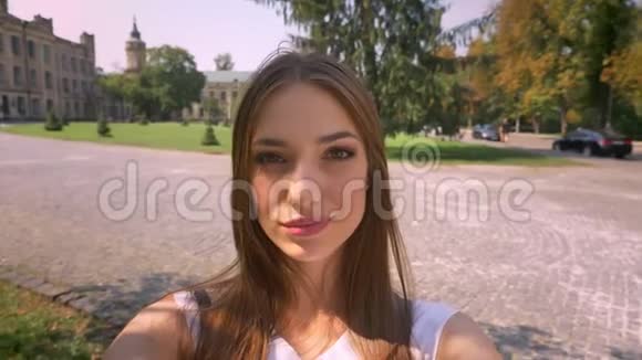 漂亮的年轻女人白天站在公园里拿着相机自拍微笑交流理念视频的预览图