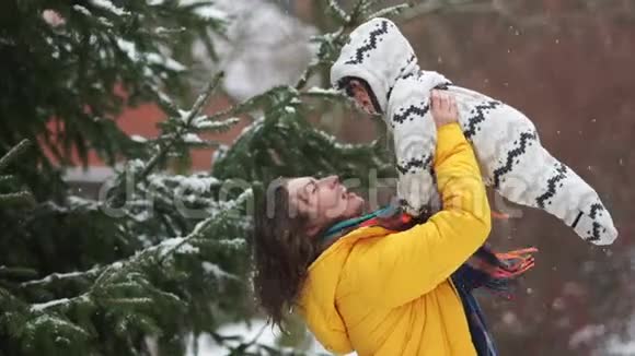 快乐的妈妈和宝宝在公园里散步下雪了女人笑着把孩子扶起来视频的预览图