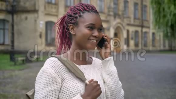 年轻漂亮的非洲学生打电话笑着背着背包站在大学附近的公园里女人和视频的预览图