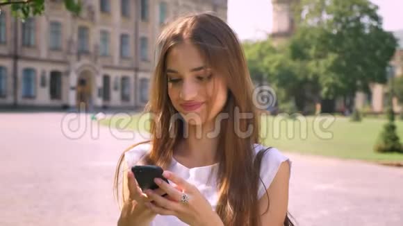 女士白天站在公园里在智能手机上输入信息看着摄像机微笑着视频的预览图