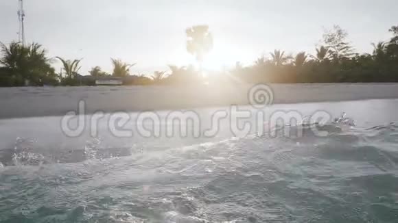 低角度背景拍摄的海浪飞溅在日落海岸与美丽的棕榈树在异国情调的海滩视频的预览图