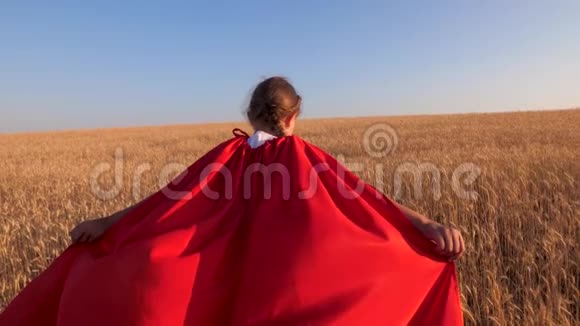女孩超级英雄跑过田野穿着红色斗篷的小麦对抗蓝天视频的预览图