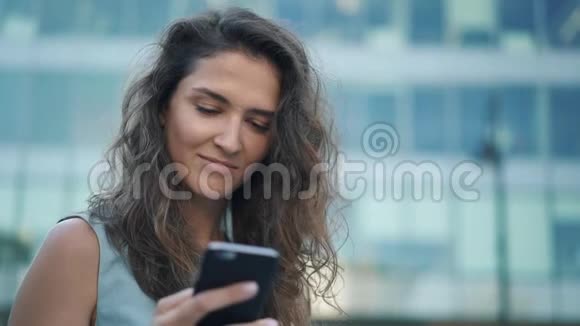 在市中心一个穿着蓝色连衣裙的漂亮年轻女孩用智能手机屏幕视频的预览图