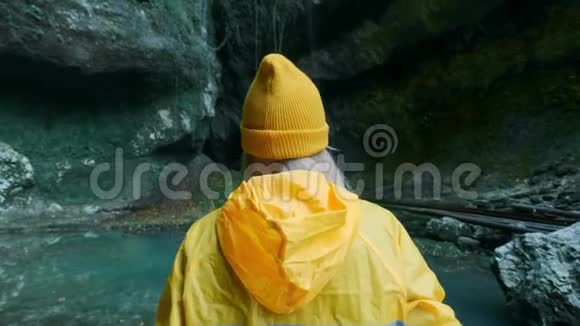 年轻美丽的白种人女孩旅行者穿着黄色雨衣穿过一个热带洞穴在这里寻找冒险视频的预览图