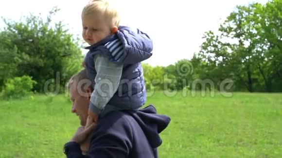 婴儿坐在他父亲的脖子上公园里父亲天视频的预览图