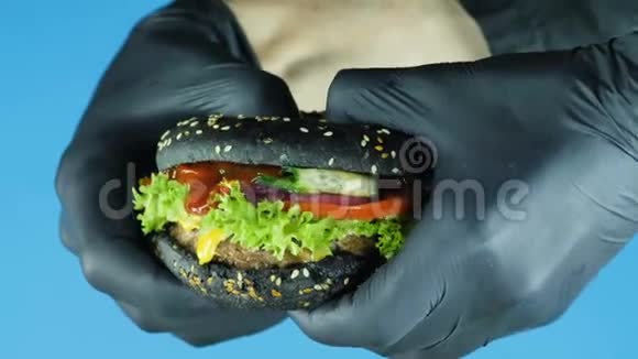 特写一只黑手套的手手里拿着一个多汁的汉堡里面夹着一个黑面包撒上芝麻和牛肉饼然后打破视频的预览图