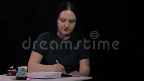 咖啡屋里的一个女人在黑色背景下喝着白色杯子里的咖啡写日记视频的预览图