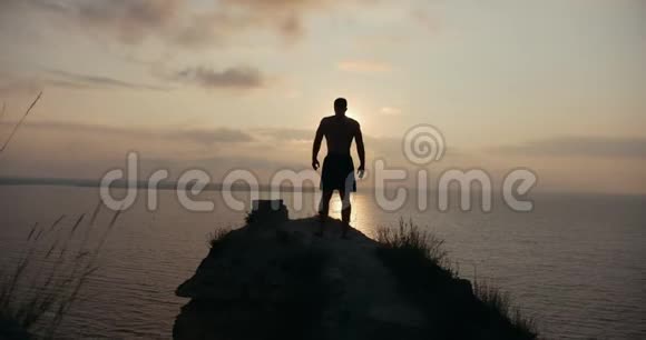 日出时在海边的大石头上蹲着的男性剪影视频的预览图