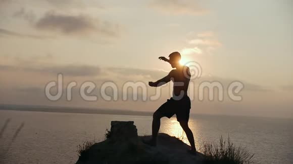 日出时在海边的大石头上做晨练的男性剪影视频的预览图