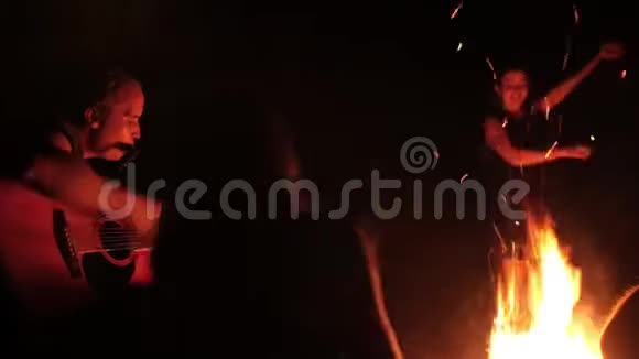 年轻朋友弹吉他女孩晚上在篝火旁跳舞视频的预览图