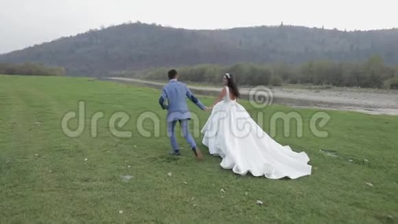 新婚夫妇在山河附近奔跑新郎和新娘相爱视频的预览图