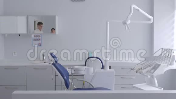 一个牙医带着一个带眼镜的年轻人走进办公室让他坐在牙科椅上视频的预览图