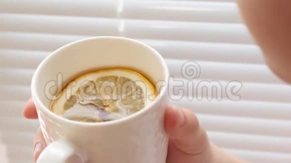 热的金茶和柠檬片在女孩手中坐在窗台附近的窗户视频的预览图